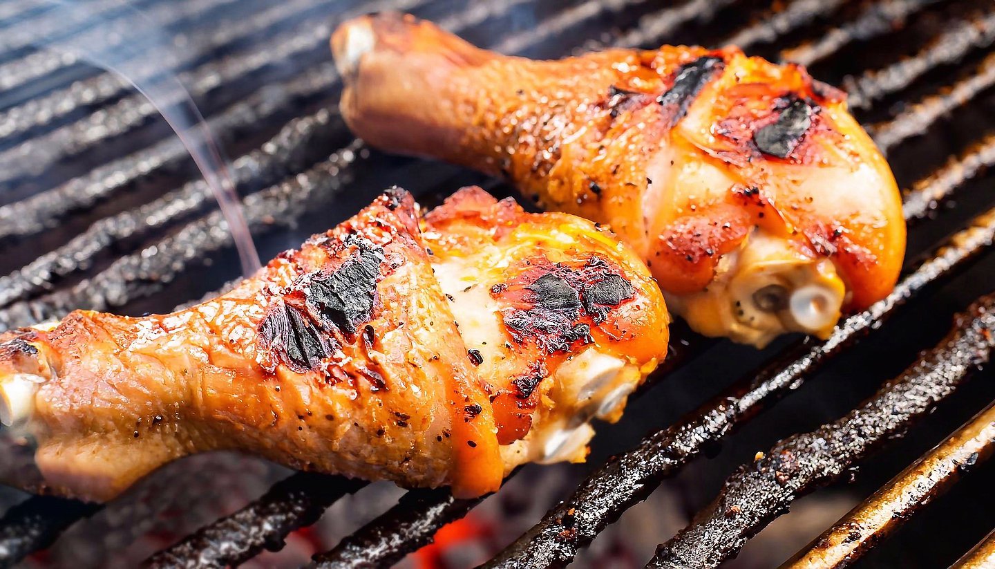Zwei Hähnchenkeulen liegen knusprig gebraten auf dem Grill in Nahaufnahme.
