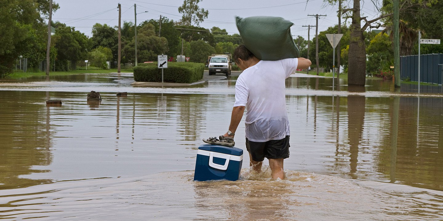 Ein Mann watet mit Gepäck durch Hochwasser.
