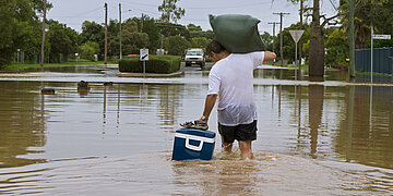 Ein Mann watet mit Gep&auml;ck durch Hochwasser.