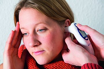 Bei einer jungen Frau wird das Fieber mit einem Ohrthermometer gemessen.