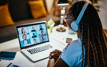 Eine Pflegekraft sitzt am Tisch mit Kopfh&ouml;rern und lernt am Laptop &uuml;ber die AOK Pflege Mediathek.