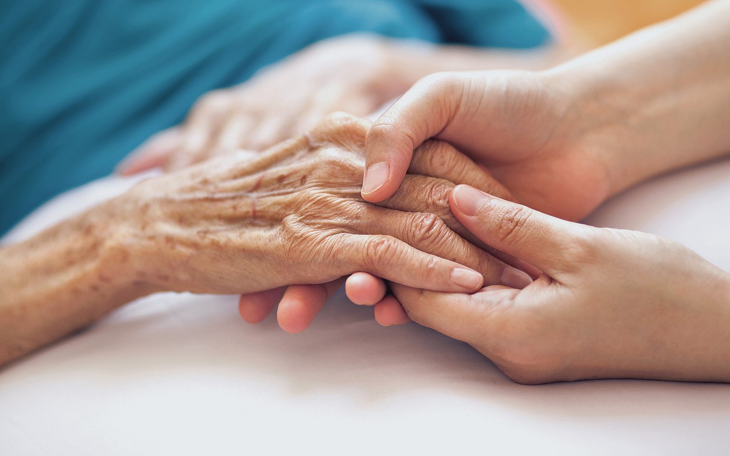 Qualitätssicherung in Pflegeheimen Foto: Zwei Hände eines jüngeren Menschen halten die Hand eines älteren Menschen.