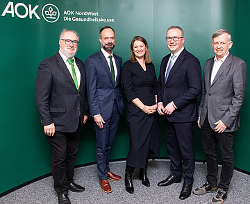 Der gew&auml;hlte Vorstand der AOK NordWest steht zusammen mit den beiden Verwaltungsratsvorsitzenden (jeweils au&szlig;en) vor gr&uuml;nem Hintergrund.