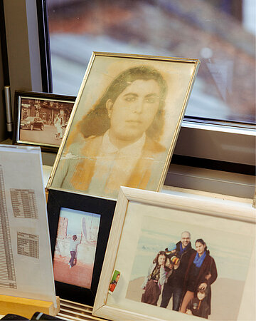 Mehrere gerahmte Familienfotos stehen auf einer Fensterbank, darunter ein &auml;lteres Portr&auml;t und ein Bild einer Familie.