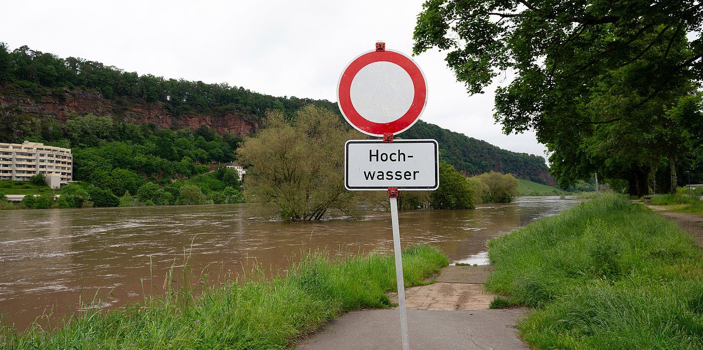 Foto: Vor einem Fluß steht ein Warnschild "Hochwasser".