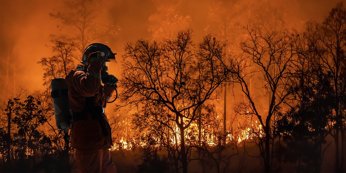Ein Feuerwehrmann steht vor einem lichterloh brennenden Waldgebiet.