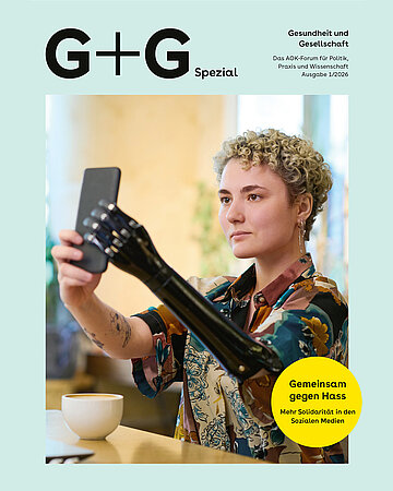 Eine Frau mit kurzen blonden Locken h&auml;lt mit ihren H&auml;nden ein Smartphone in die Luft und schaut in die Kamera. Ihr linker Arm ist eine Prothese.