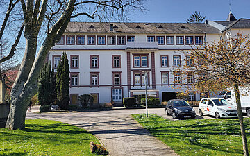 Foto: Ein Weg f&uuml;hrt zu einem dreist&ouml;ckigem Geb&auml;ude. 