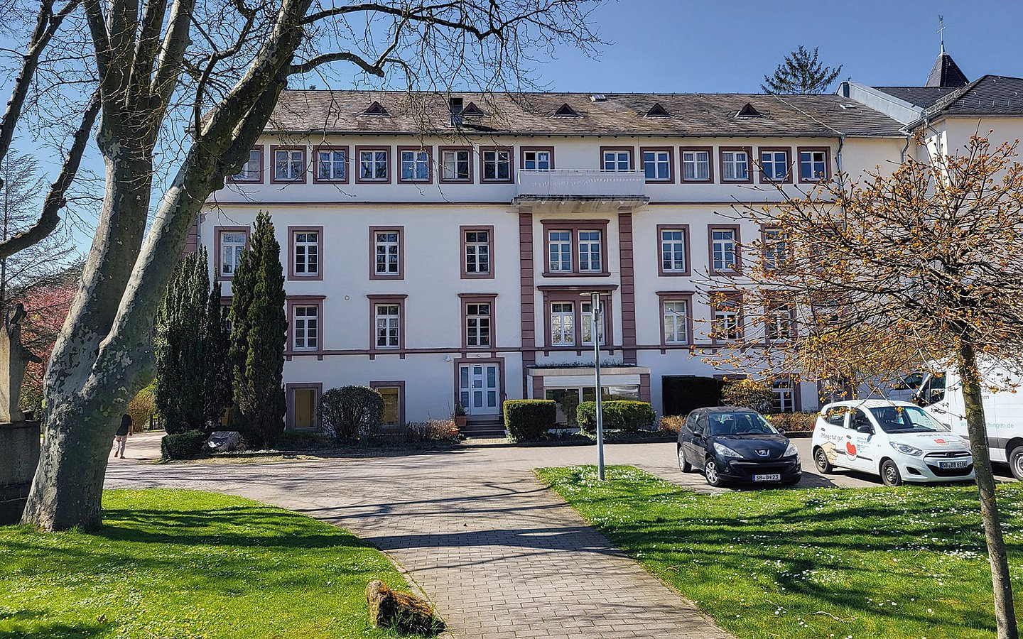 Foto: Ein Weg führt zu einem dreistöckigem Gebäude. 