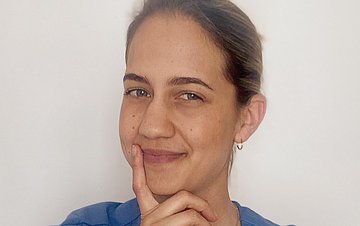 Die Gesundheits- und Krankenpflegerin Kata schaut im Portrait schräg in die Kamera und hält ihren Zeigefinger an das Kinn