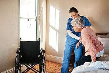 Pflegekraft hilft einer &auml;lteren Frau beim Aufstehen aus dem Bett.