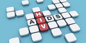 Foto: Scrabblesteine liegen nebeneinander, in Rot ist das Wort "HIV", in Wei&szlig; das Wort "Aids" gelegt.