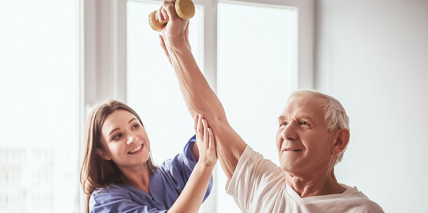 Foto einer Physiotherapeutin, die mit einem alten Mann mit einer Hantel trainiert