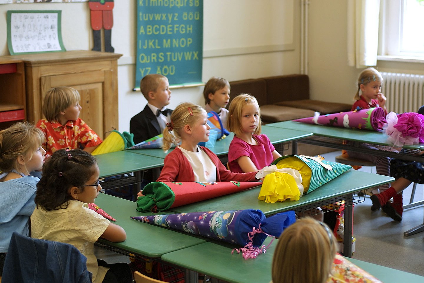 Foto: Erstklässler sitzten am ersten Schultag an ihren Tischen in der Klasse. Vor ihnen liegen Schultüten.