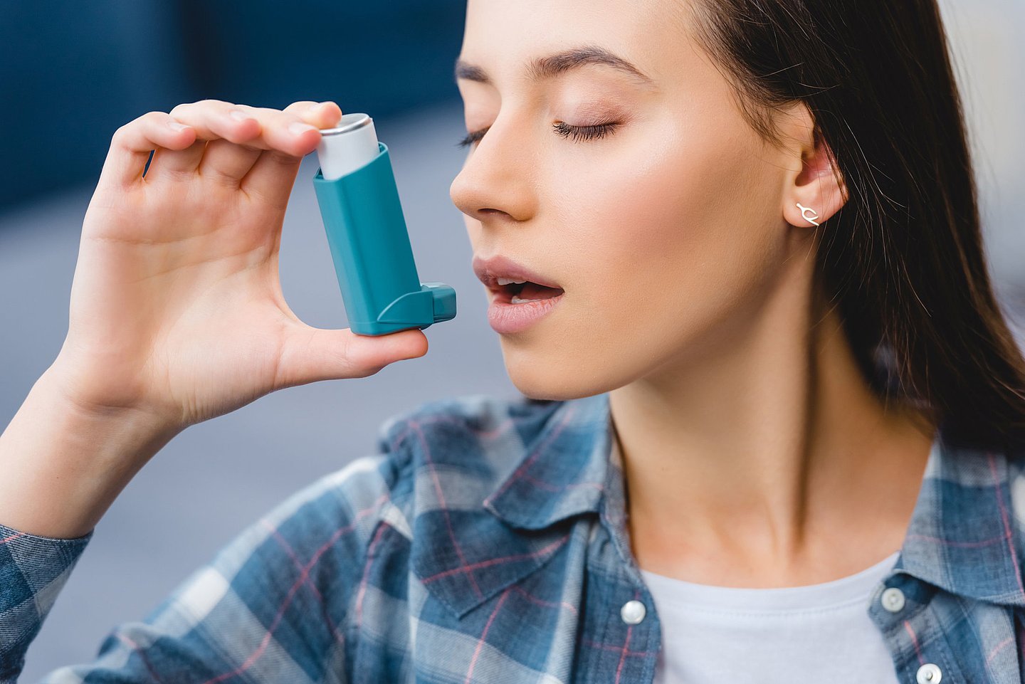 Das Foto zeigt eine junge Frau, die ein Asthma Spray anwendet.