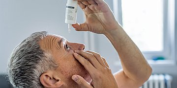 Augentropfen Ein Mann tropft sich Augentropfen in ein Auge.