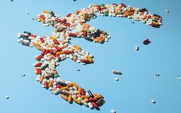 Arzneimittel Foto eines Eurozeichens, das aus Tabletten besteht vor hellblauem Hintergrund