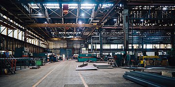 Eine große Lagerhalle mit verschiedenen Maschinen. Im Hintergrund arbeiten wenige Personen.