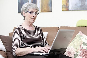 Eine ältere Frau tippt am Laptop.