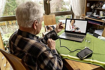 Ein &auml;lterer Herr misst seinen Blutdruck w&auml;hrend einer Videosprechstunde.