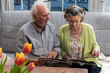 Ein &auml;lterer Mann und eine &auml;ltere Frau sitzen auf einem Sofa und schauen sich ein Fotoalbum an.