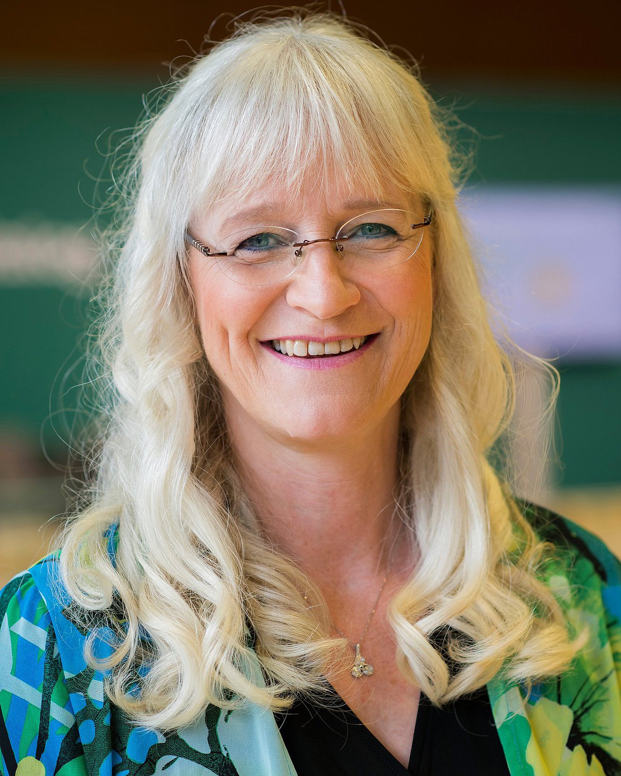 Porträtfoto: Susanne Strombach, Frau mittleren Alters, blond, Brille, blau-grüne Bluse in Batik-Optik