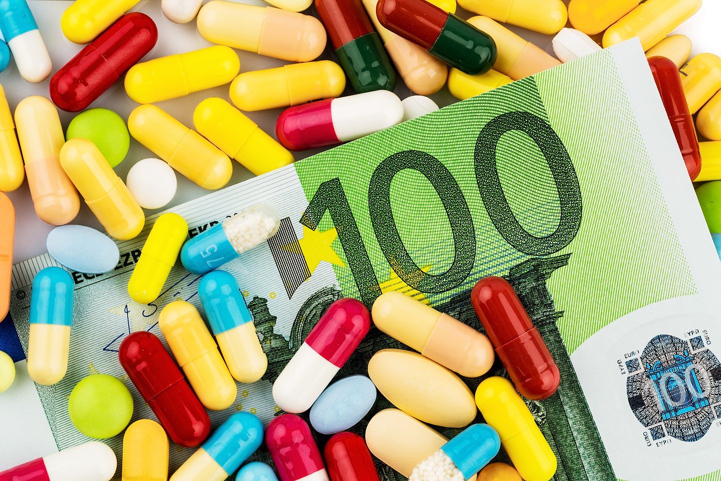 Auf dem Foto ist ein 100 Euro-Schein mit vielen verschiedenen Tabletten abgebildet.