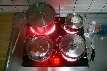 Elektroherd Vier Töpfe stehen auf einem Elektroherd, dessen Heizplatten rot aufglühen.