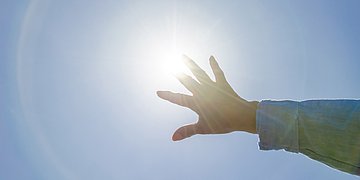 Foto: Eine Hand reckt sich in den Himmel Richtung Sonne.