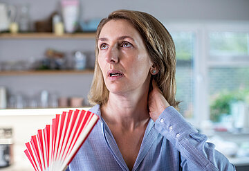 Eine Frau wedelt sich mit einem F&auml;cher in der Hand Luft ins Gesicht.