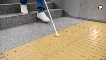 Eine sehbehinderte Person geht eine Treppe hinab. Nur die Beine und ein wei&szlig;er Gehstock sind zu erkennen.