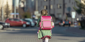 Ein M&auml;dchen mit Schulranzen l&auml;uft durch die Stra&szlig;e.