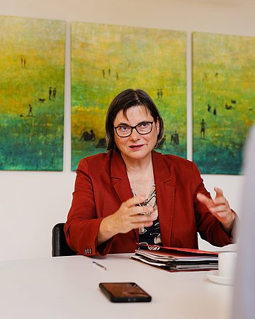 Foto: Christine Fuchsloch, Präsidentin des Bundessozialgerichtes (BSG), sitzt an einem Schreibtisch und gestikuliert mit ihren Händen.