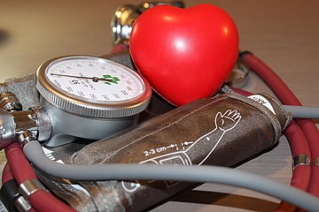 Blutdruckmessgerät Ein rotes Herz aus Plastik liegt neben einem Blutdruckmessgerät.
