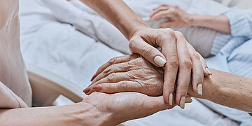 Bild: Eine Hand h&auml;lt die Hand einer anderen, auf einem Bett liegenden Person.
