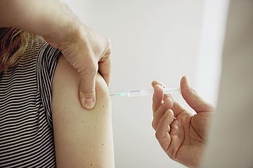 Impfung Eine junge Frau wird mit einer Spritze in den Arm geimpft