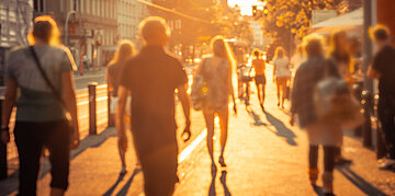Foto: Menschen gehen bei tief stehender Abendsonne durch eine belebte Innenstadt.