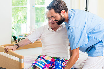 Das Foto zeigt einen Pfleger im Pflegeheim, der einem Pflegebed&uuml;rftigen aus dem Bett hilft.
