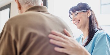 Pflegereform Foto: Pflegerin mit Schutzbrille stützt alten Mann