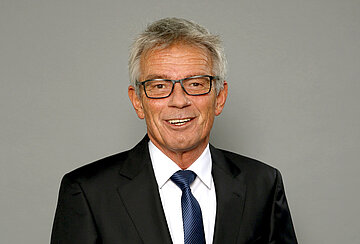 Das Portr&auml;tfoto zeigt einen Mann mit Brillie, blauem Sakko, wei&szlig;em Hemd und blauer Krawatte.