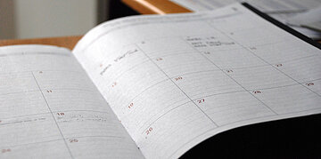 Aufgeschlagener Papier-Terminkalender mit Monats&uuml;bersicht und eingetragenen Notizen.