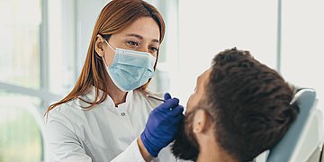 Mundgesundheit Auf einem Zahnarztstuhl sitzt ein Mann, während ihn die Zahnärztin behandelt.
