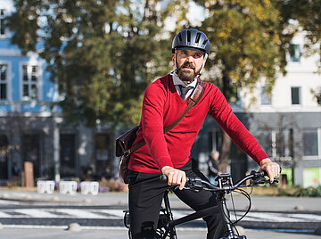 Ein Mann sitzt auf seinem Fahrrad und f&auml;hrt durch eine Stra&szlig;e.