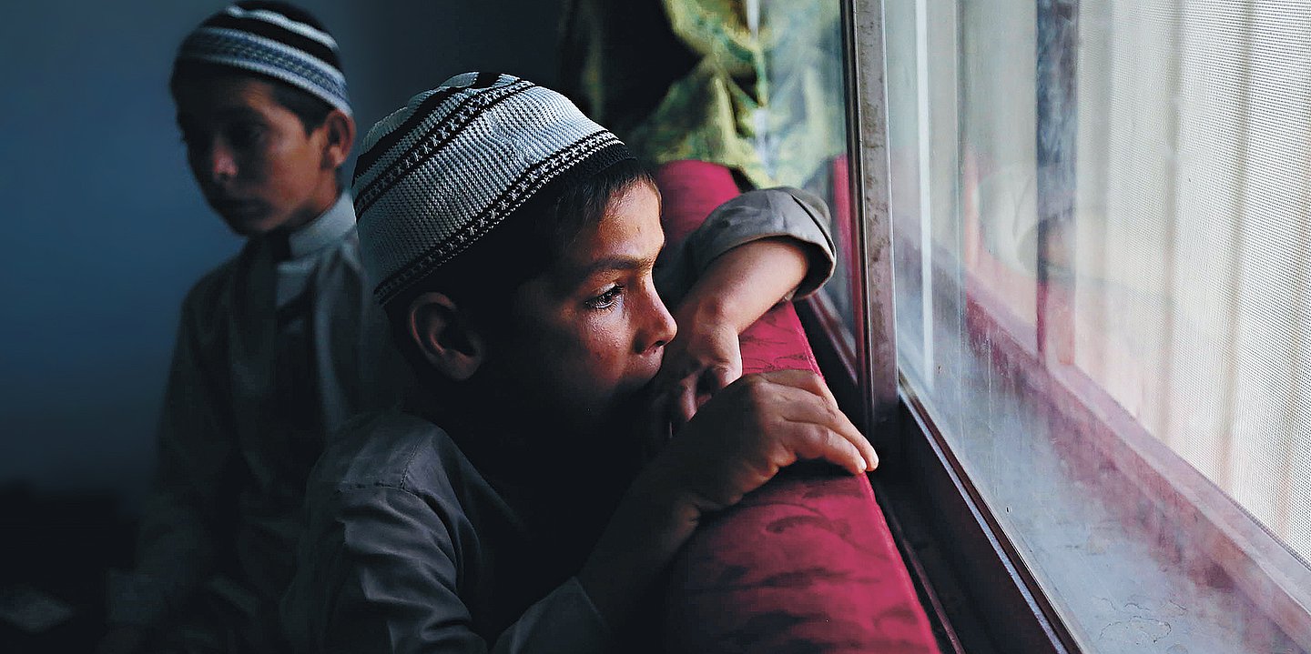 Foto von zwei traditionell gekleideten pakistanischen Jungen auf einem roten Sofa