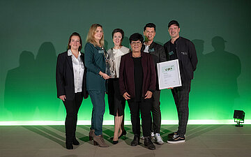 Foto: 6 Personen stehen nebeneinander, eine h&auml;lt eine Urkunde. 