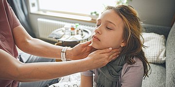 Pfeiffersches Drüsenfieber Eine Frau tatstet einem jungen Mädchen die Lymphknoten am Hals ab.