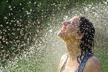 Erfrischende Abkühlung Das Foto zeigt eine Frau in einem Wasserschauer.