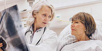 Symbolbild einer &Auml;rztin, die einer Frau in einem Krankenhausbett ein R&ouml;ntgenbild erkl&auml;rt