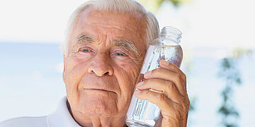 Foto: Ein &auml;lterer Mann h&auml;lt sich eine Wasserflasche an die Wange.
