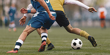 Foto: Zwei Fu&szlig;ballspieler auf dem Fu&szlig;ballfeld k&auml;mpfen um den Ball.